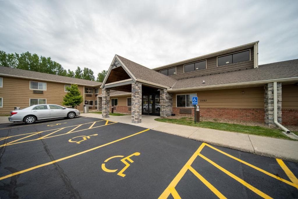 Tan hotel entrance featuring a stone-pillared portico and yellow-marked accessible parking spots in front.